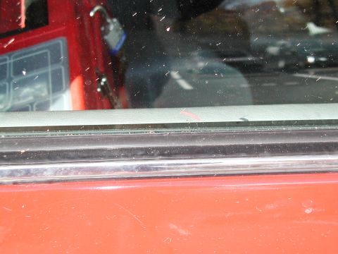 1992 Ford Taurus - Close-up of a red car's interior door panel and window, showing a reflection of the road and passing vehicles.