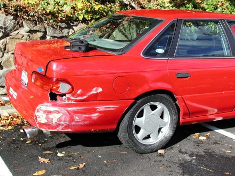1992 Ford Taurus - This red sedan has significant damage to its rear bumper and taillight assembly.