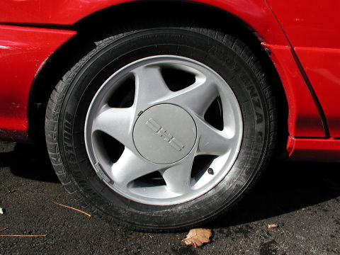 1992 Ford Taurus - A close-up view of a red car's wheel and tire, with visible text on the tire sidewall.