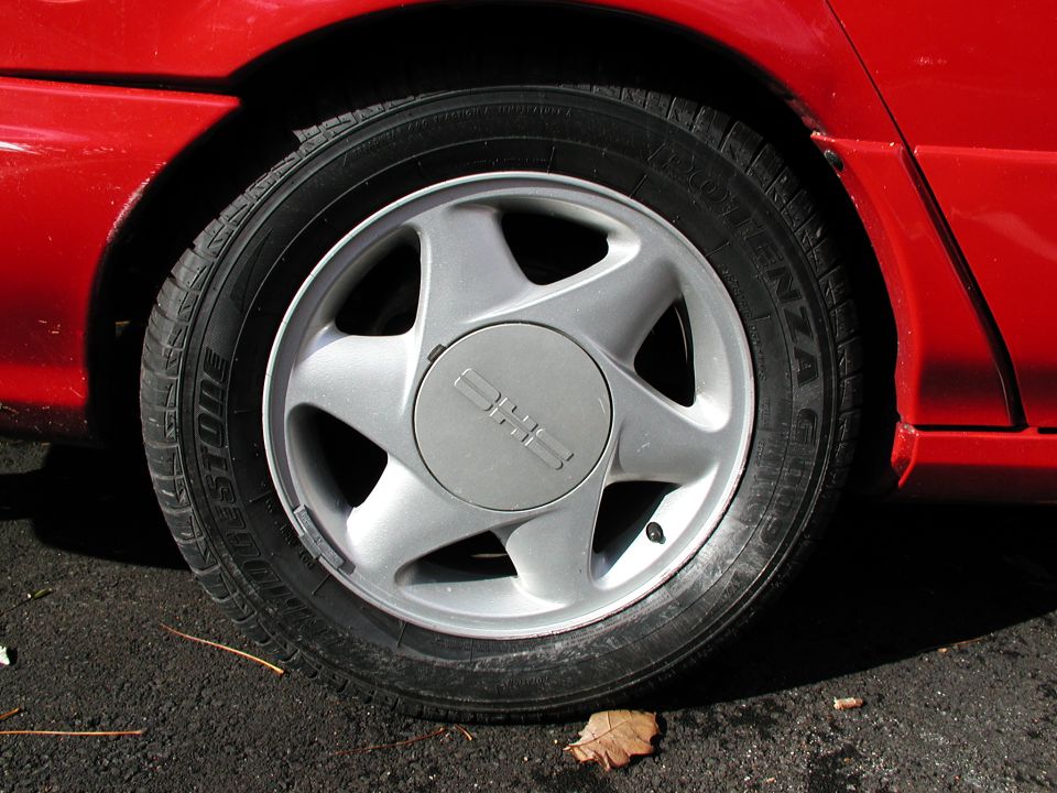 Red car's silver five-spoke wheel with a 'GMC' logo on the hubcap, showing a Bridgestone tire