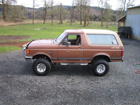 1991 Ford Bronco - This lifted 1992 Ford Bronco has a two-tone brown and tan exterior and is shown from the side.