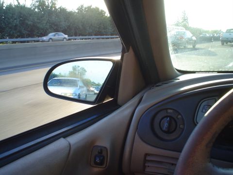1993 Ford Taurus - View from inside a car shows traffic on a highway, with a light-colored sedan reflected in the passenger side mirror.