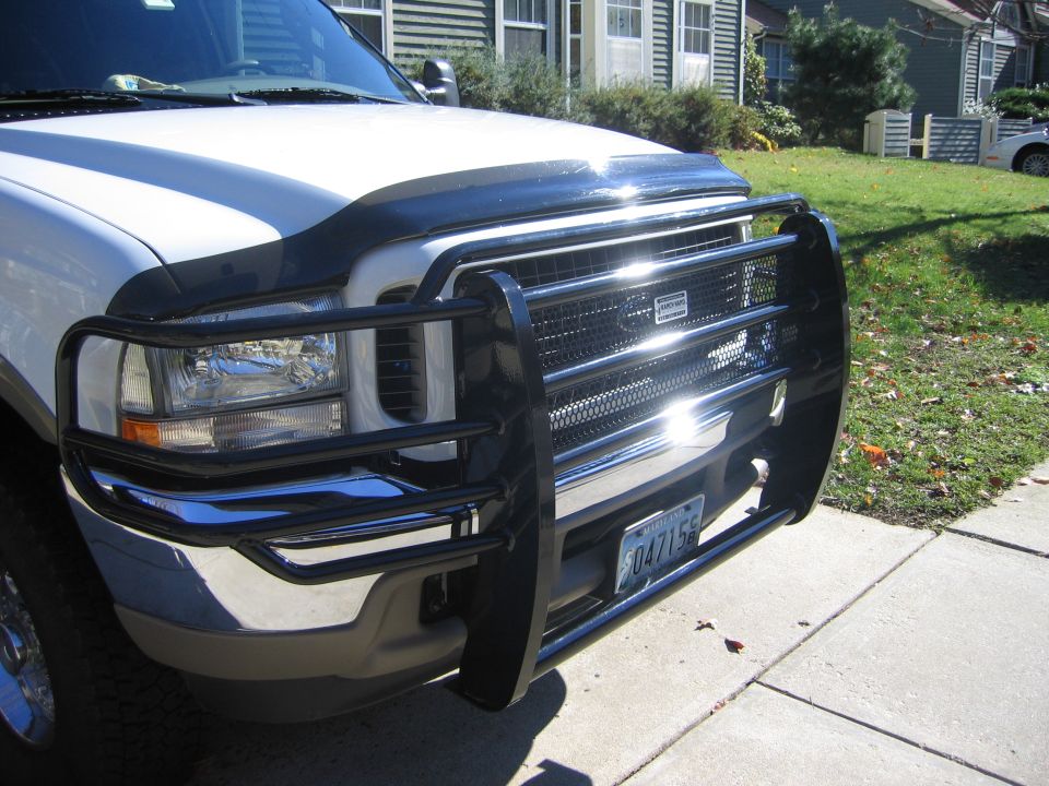 White Ford truck front end with black tubular grille guard and hood deflector on a driveway