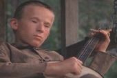 1991 Ford Bronco - A young boy is focused on playing a stringed instrument, possibly a mandolin or ukulele, while sitting outdoors.