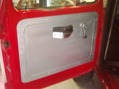 1978 Ford Bronco - Close-up of a vehicle's interior door panel, a custom aluminum insert, armrest, and window crank.