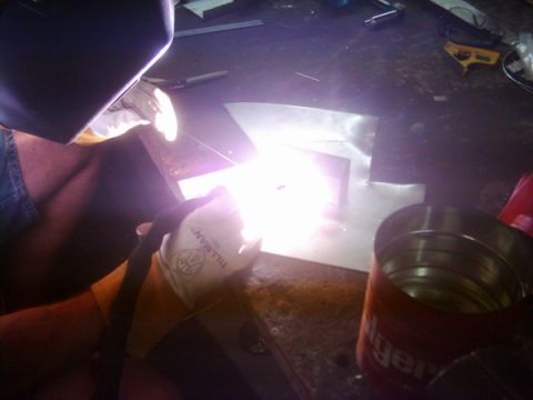 1978 Ford Bronco - A person welds metal sheets in a workshop, with a can visible in the foreground.