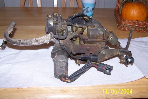 1979 Ford Bronco - A worn carburetor, likely from an older vehicle, is displayed on a wooden table.