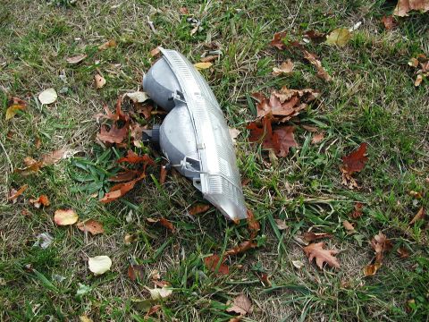 1992 Ford Taurus - A detached headlight assembly rests on the ground amidst fallen autumn leaves.