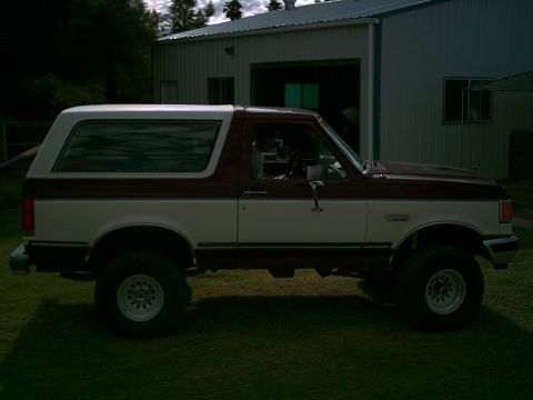 1988 Ford Bronco - Side view of a two-tone maroon and white 1988 Ford Bronco parked on grass.
