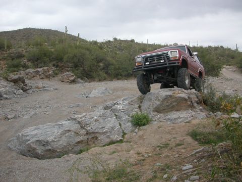 1984 Ford Bronco - This 1984 Ford Bronco is shown off-roading on a rocky trail in a desert landscape.