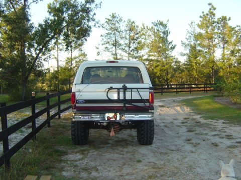1993 Ford Bronco - Rear view of a 1993 Ford Bronco parked on a dirt road with a wooden fence.