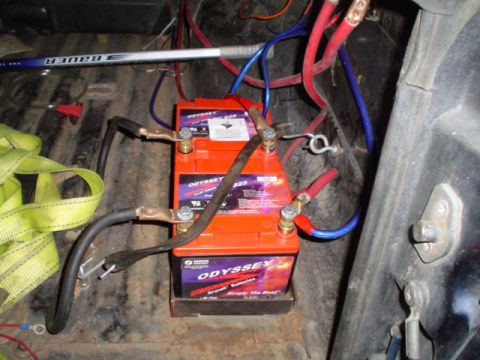 1981 Ford Bronco - Three orange Odyssey Drycell batteries strapped into a bed-mounted tray with heavy welding-cable jumpers, brass battery terminals and thick…