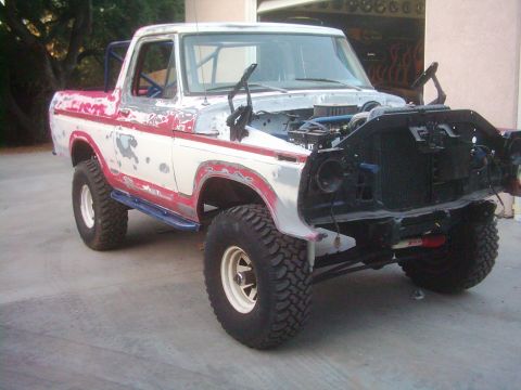 1978 Ford Bronco - A white and red 1978 Ford Bronco is shown with its hood open and front end disassembled, revealing the engine bay.