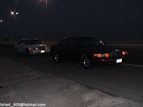 2000 Ford Crown Victoria - Two 2000 Ford Crown Victorias are seen driving on a road at night, captured from a 3/4 front view.