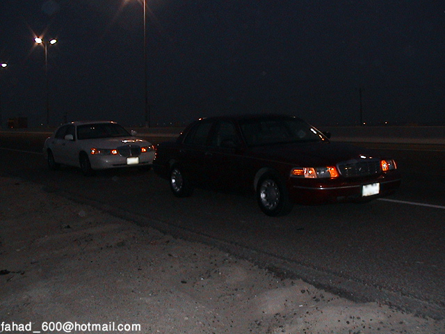 Two 2000 Ford Crown Victorias driving at night, front 3/4 view