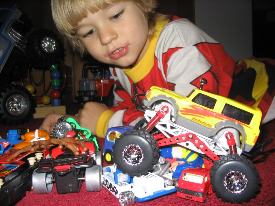 Child playing with multiple toy monster trucks on a red carpet