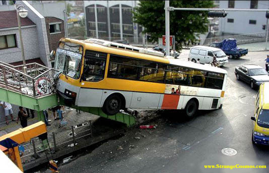 Yellow and white bus crashed onto a pedestrian overpass, front end damaged, side windows intact