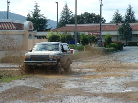 1990 Ford Bronco - Ford Bronco kicks up mud while driving through a wet, unpaved area.