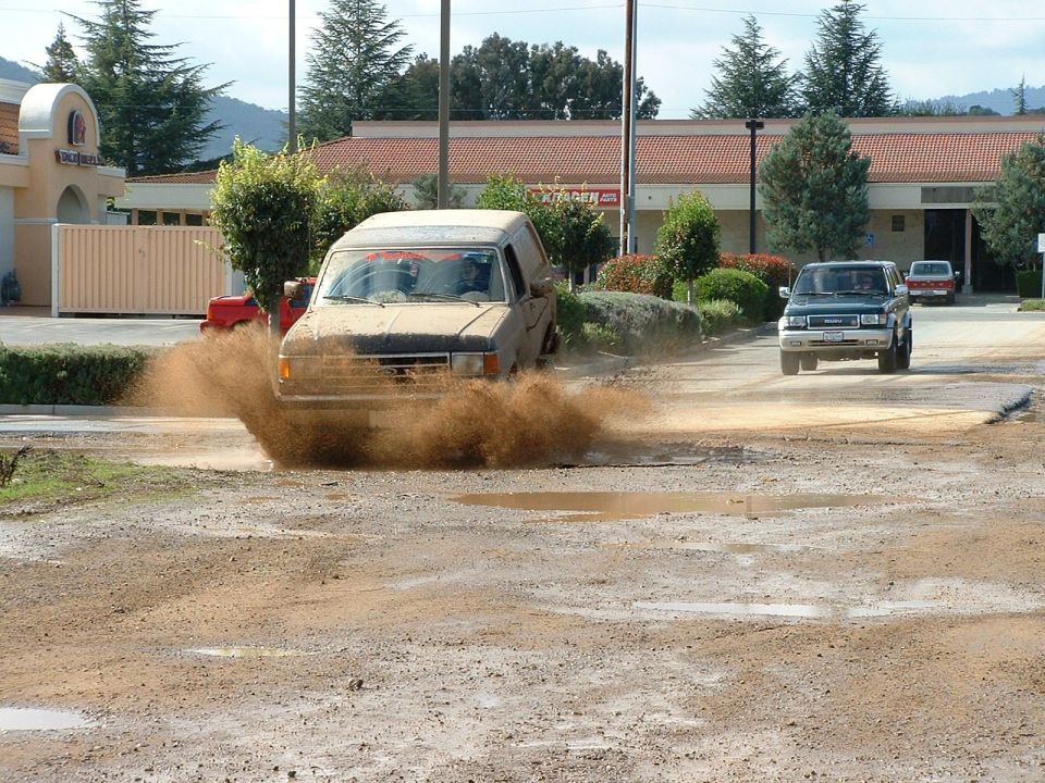 Muddy van driving through a puddle, kicking up dirt