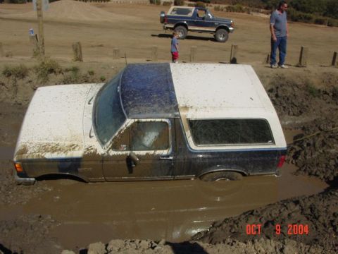 1990 Ford Bronco - A Ford Bronco is stuck in the mud while another Bronco watches from higher ground.