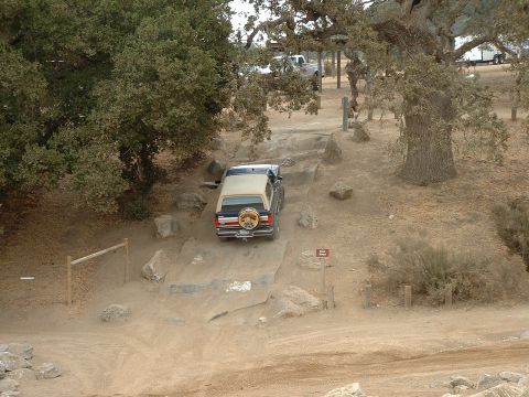 1990 Ford Bronco - A Ford Bronco navigates a rocky off-road trail under large oak trees.