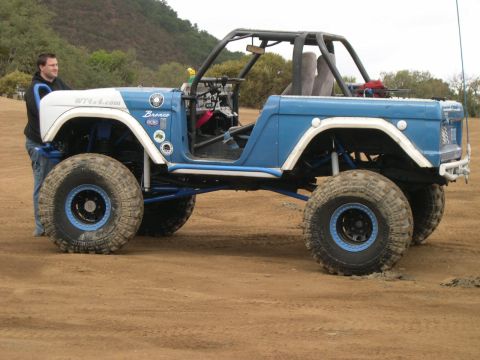 1990 Ford Bronco - Modified off-road vehicle with a roll cage and oversized tires sits on a dirt surface.