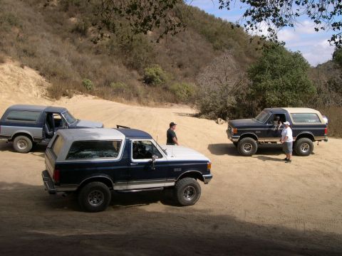 1990 Ford Bronco - Three Ford Bronco SUVs are parked on a dirt road in a hilly, arid landscape.