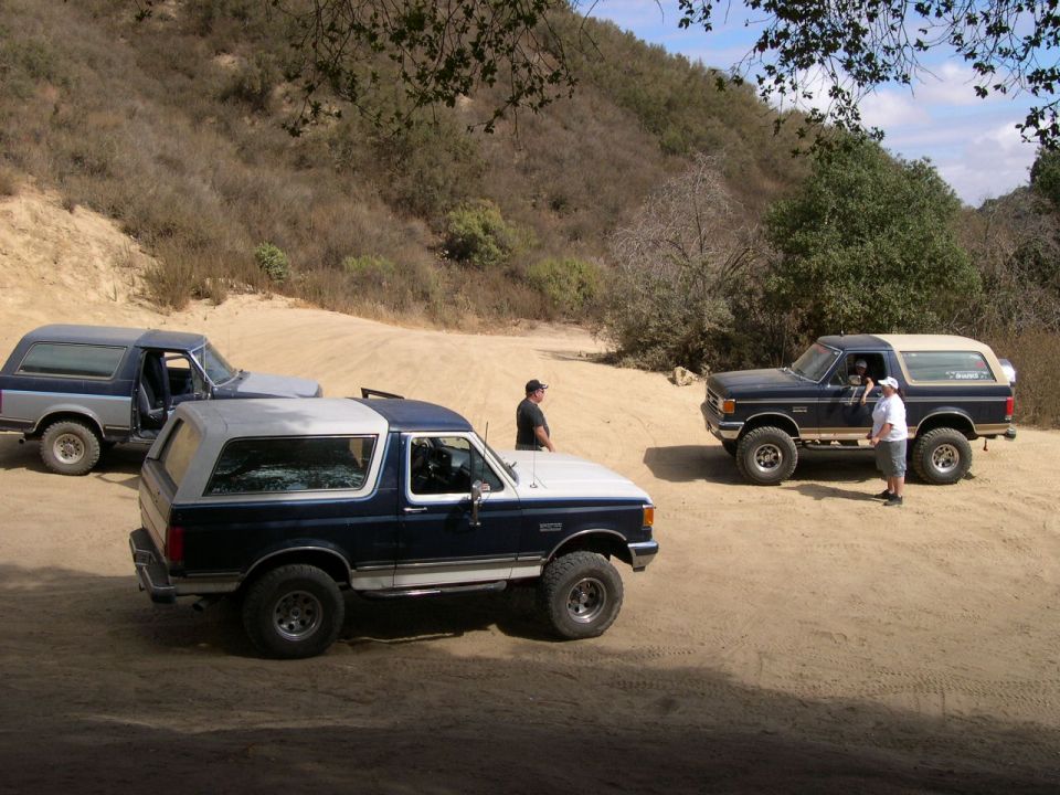 Three Ford Bronco SUVs parked on a dirt road with hills in the background