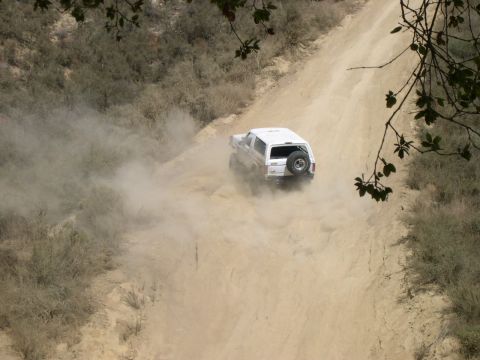 1990 Ford Bronco - A white 1990 Ford Bronco navigates a dusty dirt road, kicking up a cloud of dust as it drives away.