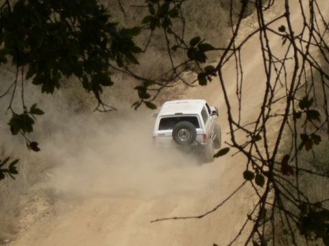 1990 Ford Bronco - White 1990 Ford Bronco navigates a dusty dirt road, seen from behind.
