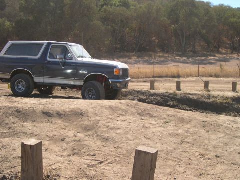 1990 Ford Bronco - A lifted Ford Bronco navigates an off-road course with a wooded area in the background.