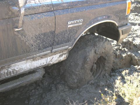 1990 Ford Bronco - A 1990 Ford Bronco is deeply stuck in mud, with its side and large tire covered in thick mud.