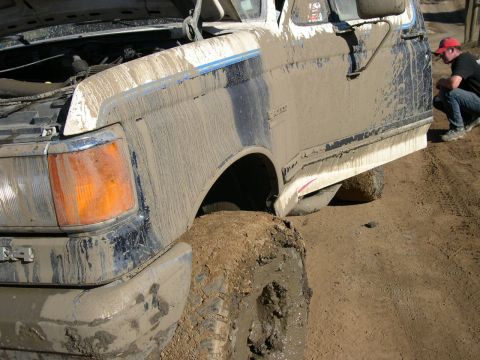 1990 Ford Bronco - Mud-covered 1990 Ford Bronco stuck in dirt with a person watching.