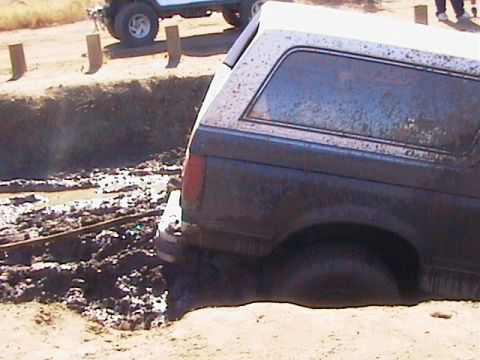 1990 Ford Bronco - This 1990 Ford Bronco appears to be stuck in a muddy ditch, with another vehicle nearby.