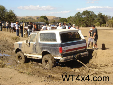 1990 Ford Bronco - A group of people watch as a Ford Bronco navigates a muddy obstacle course.
