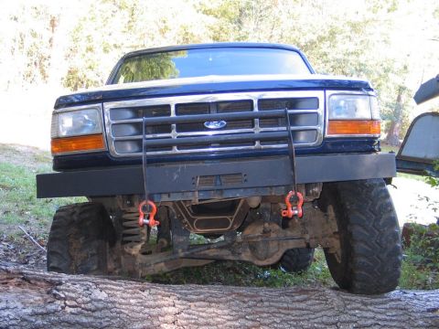 1995 Ford Bronco - This blue Ford F-Series truck features a heavy-duty bull bar and off-road tires, positioned on a fallen tree.