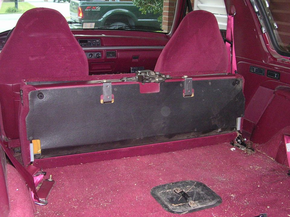 Rear interior of a Bronco with maroon carpet, rear seat removed showing black seat-back panel and floor access panel