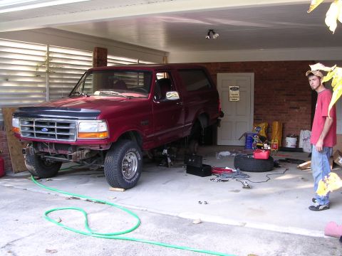1995 Ford Bronco - A maroon Ford Bronco is being worked on in a garage, with its front end elevated on jack stands.