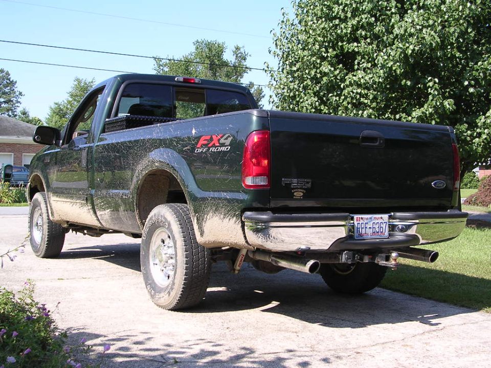 Muddy dark green Ford F-250 FX4 regular cab pickup, rear three-quarter view in a driveway