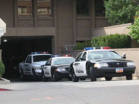 1992 Ford Crown Victoria - Multiple police vehicles, including a black and white Ford Crown Victoria, are lined up outside a building.