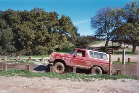 1978 Ford Bronco - A red and white 1978 Ford Bronco navigates a muddy obstacle course marked by wooden posts.