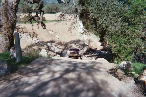 1978 Ford Bronco - A red pickup truck navigates a rough, dusty terrain surrounded by natural landscape elements.