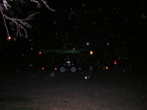 1995 Ford Bronco - A dark SUV is visible at night with its taillights illuminated. The scene is dark with some branches in the foreground.