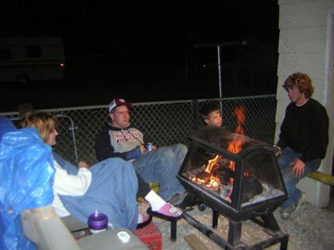 1995 Ford Bronco - A group of people gather around a fire pit on a dark night, with a trailer parked nearby.