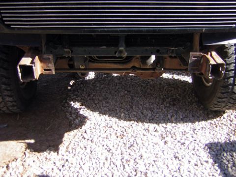 1995 Ford Bronco - Close-up view of the front bumper mounts and grille of a vehicle, with gravel on the ground.