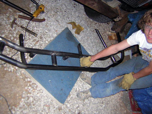 Black metal custom bumper assembly on blue mat, with tools and a person in jeans and gloves