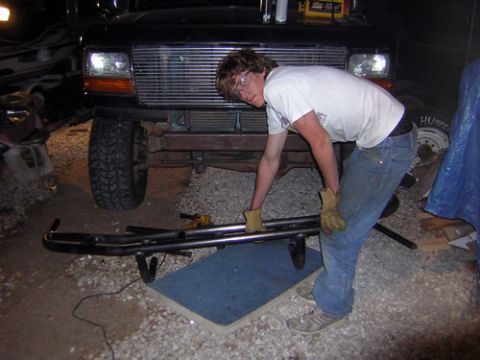1995 Ford Bronco - A person works on a custom bumper in front of a 1995 Ford Bronco, highlighting its front grille and headlights.