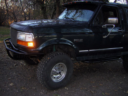 Dark green lifted Ford Bronco SUV, front 3/4 view with tube bumper and off-road tires