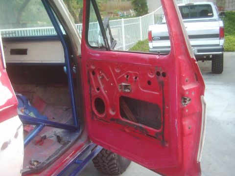 1978 Ford Bronco - Interior view of a vehicle's red door, with a white pickup truck visible in the background.