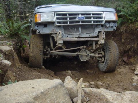 1987 Ford Bronco - A 1987 Ford Bronco navigates a challenging off-road course with its front end angled towards the viewer.